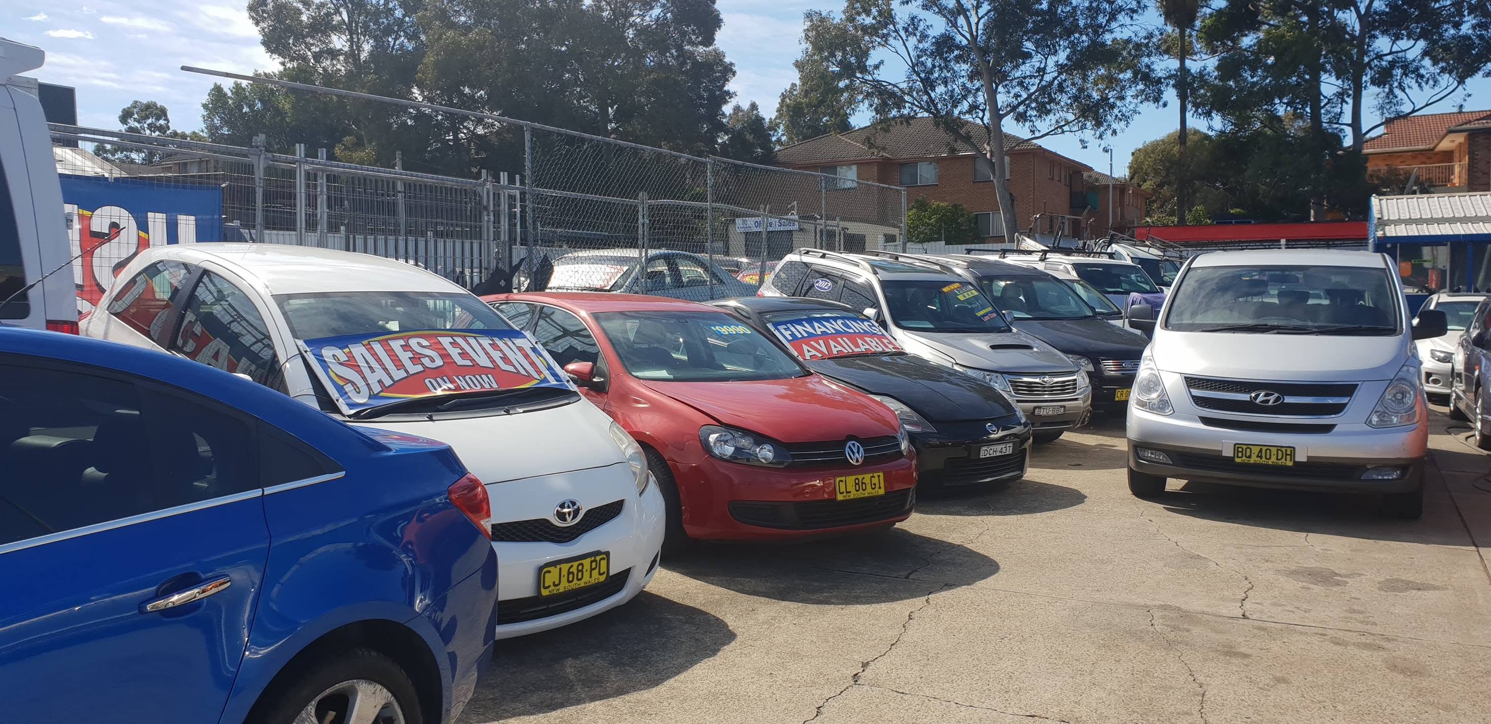 Cars nose-in on the yard: a white Yaris, a red Golf, a black Nissan, a Subaru Forester and a silver Hyundai iMax