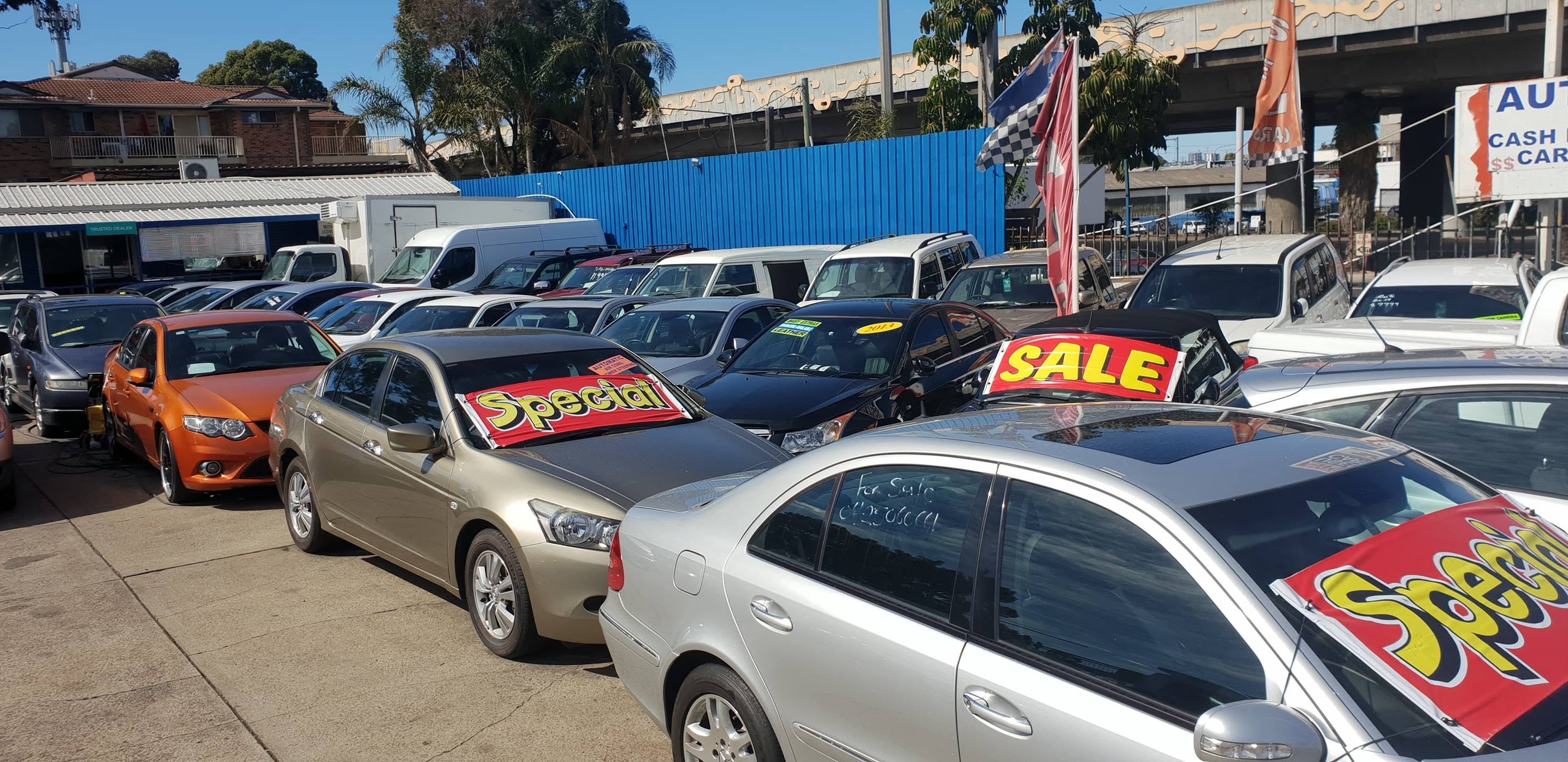 Special and Sale boards on the windscreens deeper into the yard, with a Falcon XR6, a Honda Accord and a Mercedes-Benz